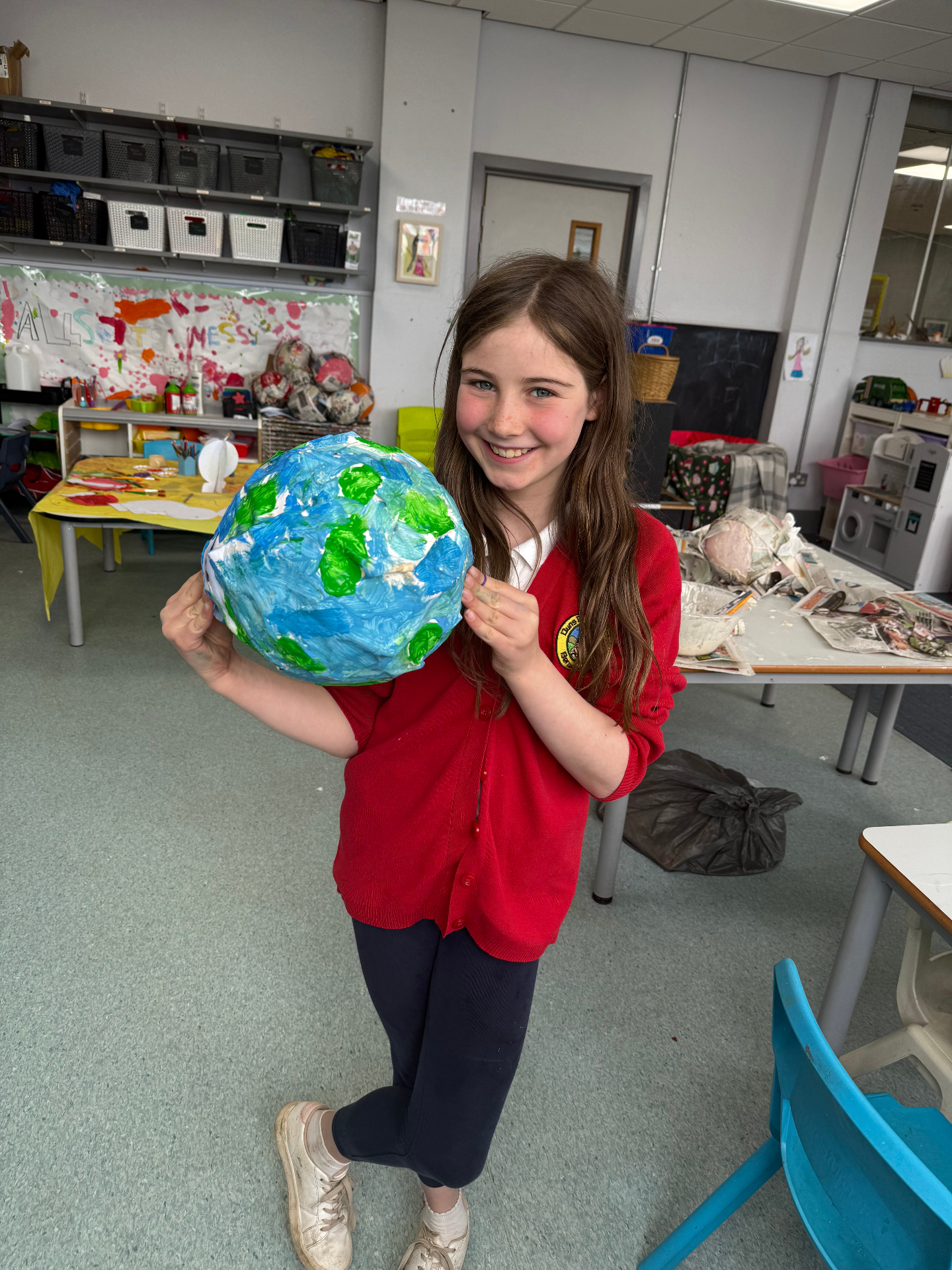 Child proudly holding a handmade globe craft at AllSorts